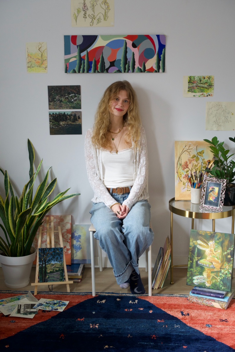 Fiamma Franchetti Bond sitting on a stool in her studio, surrounded by her paintings and plants