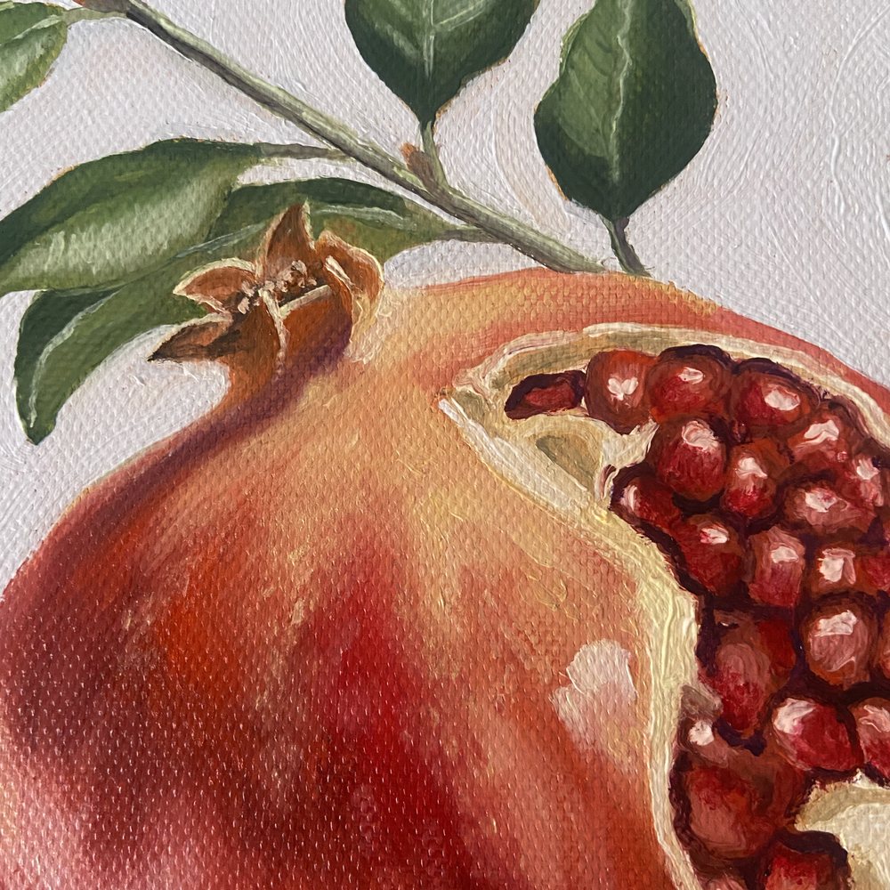 Close-up of the whole pomegranate with its crown, a branch of leaves above