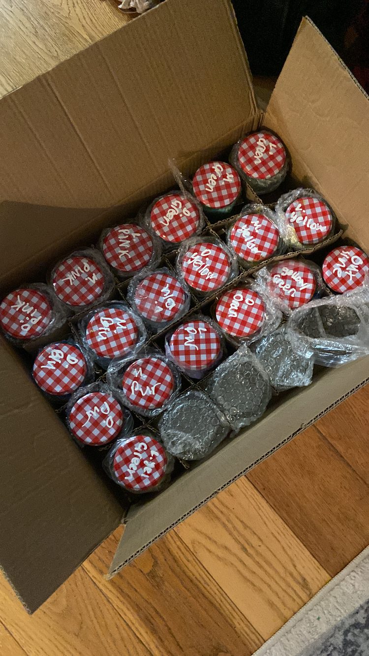 A box of jam jars with gingham lids, each labelled with the colour mixed inside